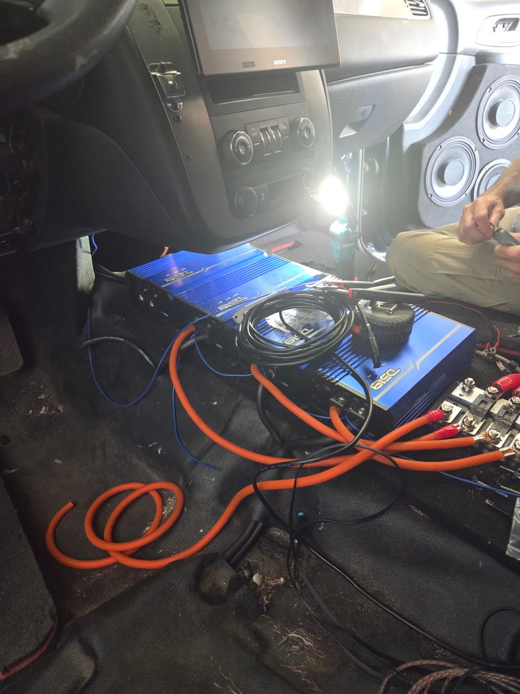 Amplifiers and orange power cable running through the Tahoe's front floor with the Sony radio in the dash