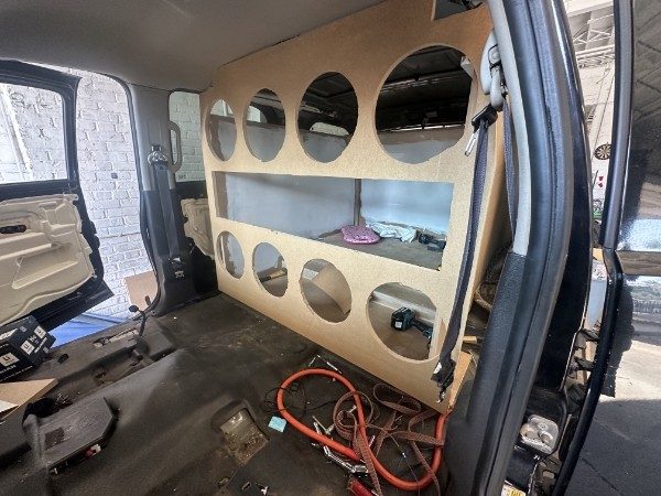 Subwoofer wall installed behind the front seats with eight cutouts and an open port window